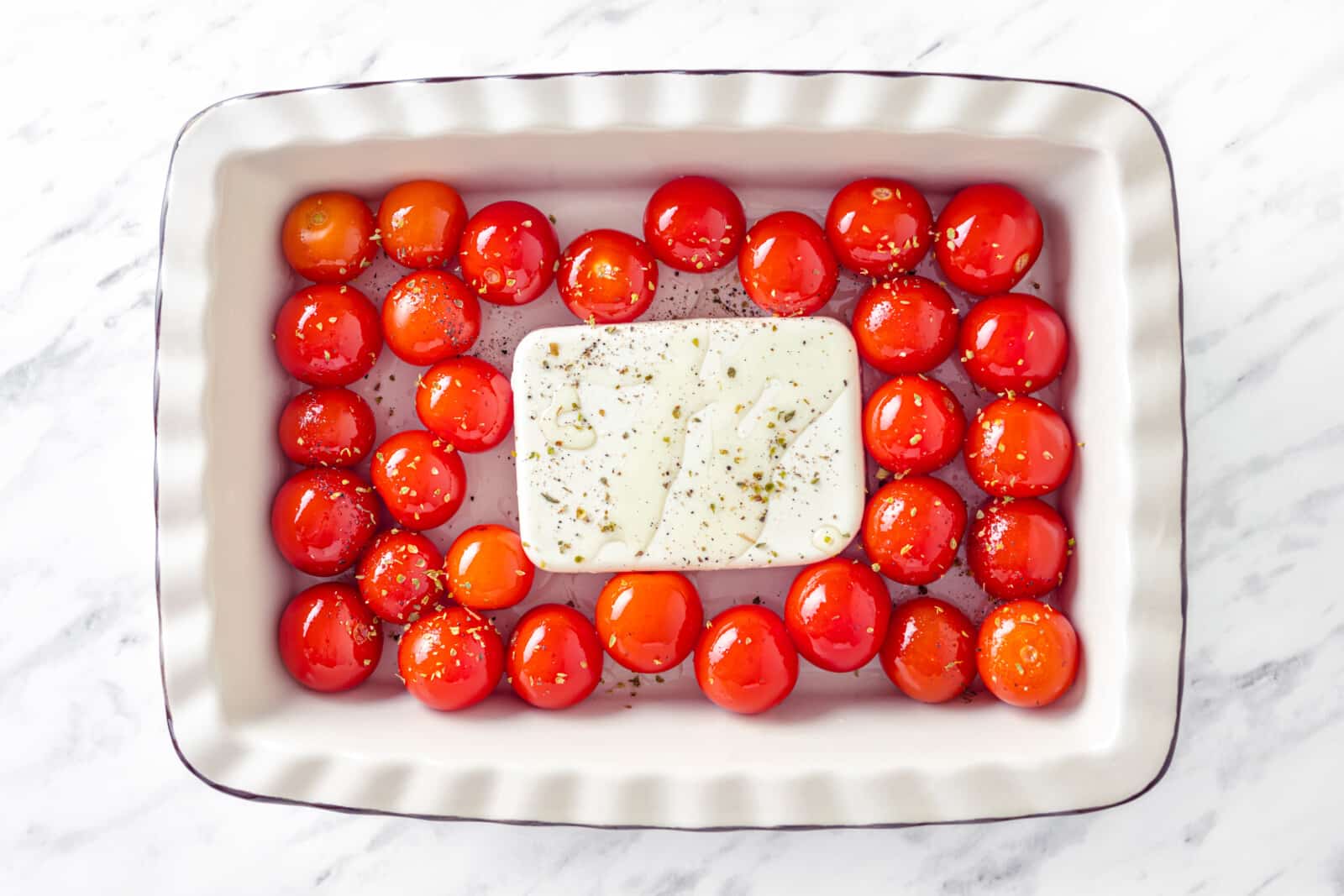 uncooked cherry tomatoes and a block of feta cheese in a white baking dish 