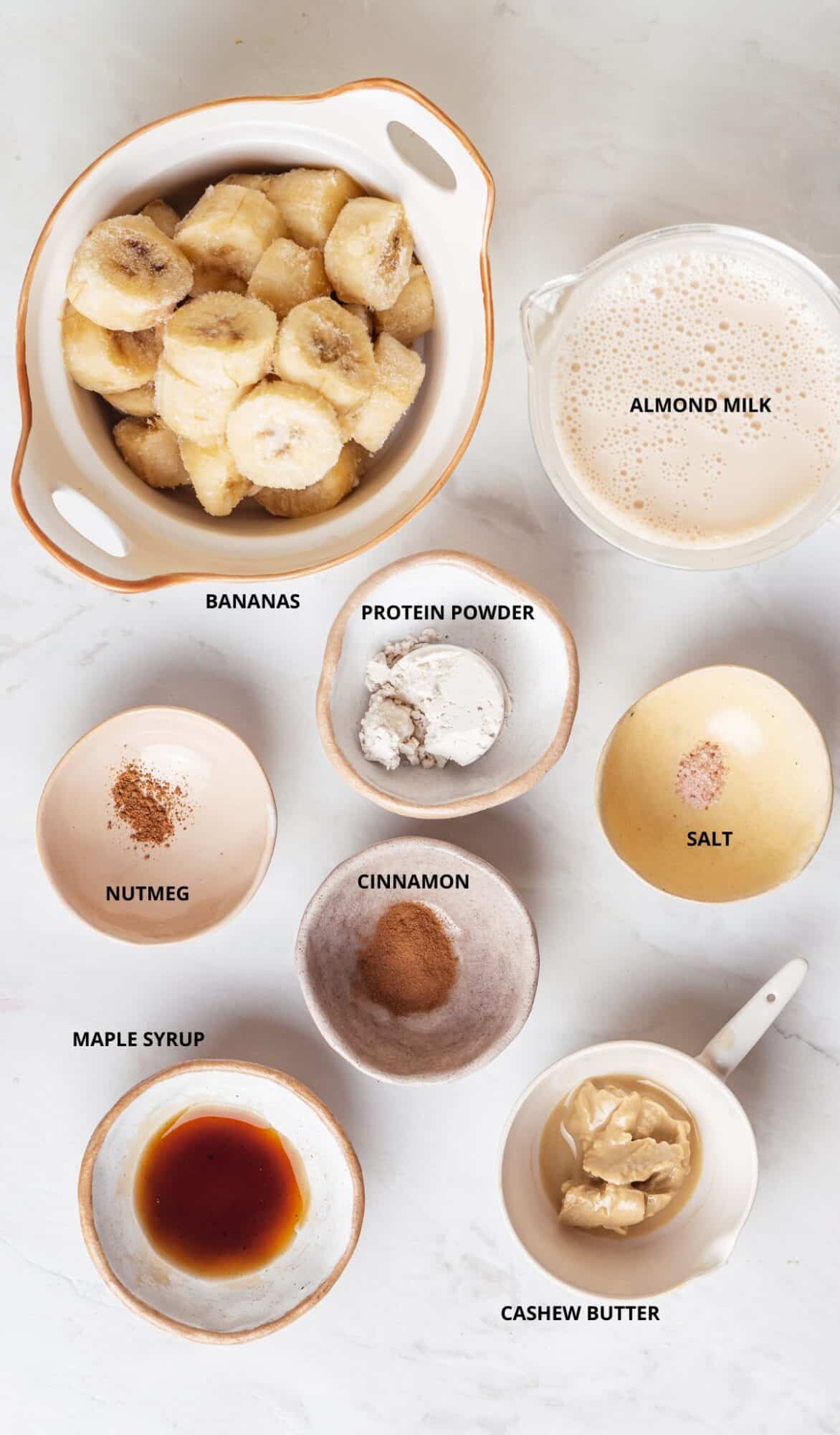 Banana bread protein smoothie ingredients- bananas, almond milk, cashew butter, maple syrup, nutmeg, cinnamon, protein powder, and salt.