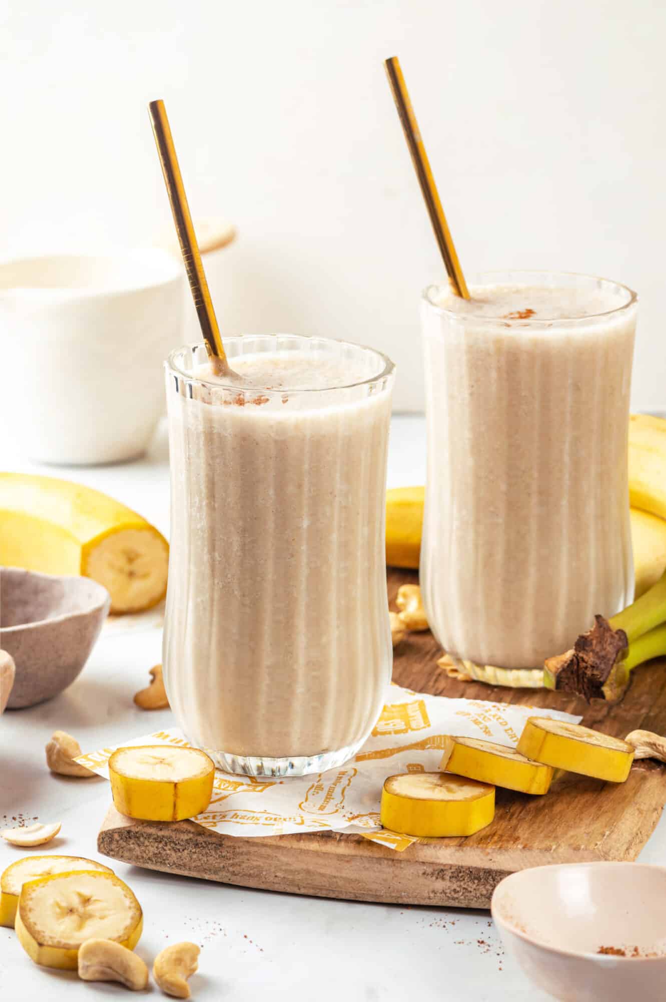 Banana bread smoothie atop a wooden board with cashews and bananas on the side.