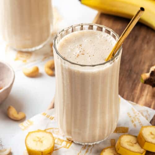 Banana protein smoothie with a gold straw, and bananas on the side.