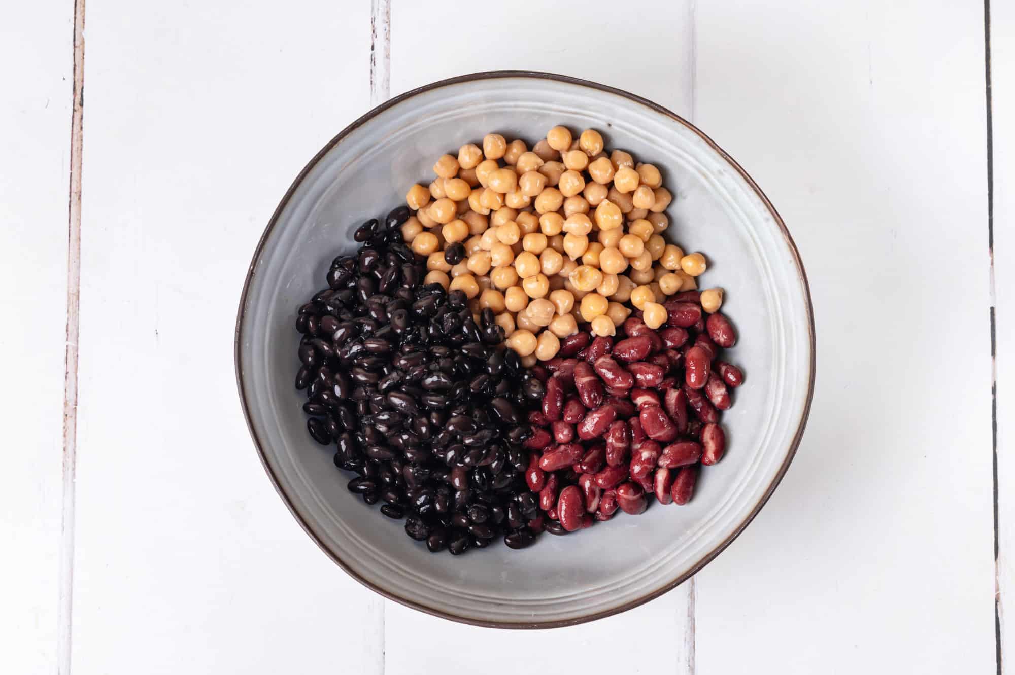 a bean selection separated in a grey bowl with a thin brown rim.