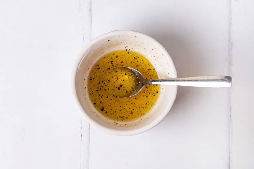 a small white bowl with dressing and a spoon in it.