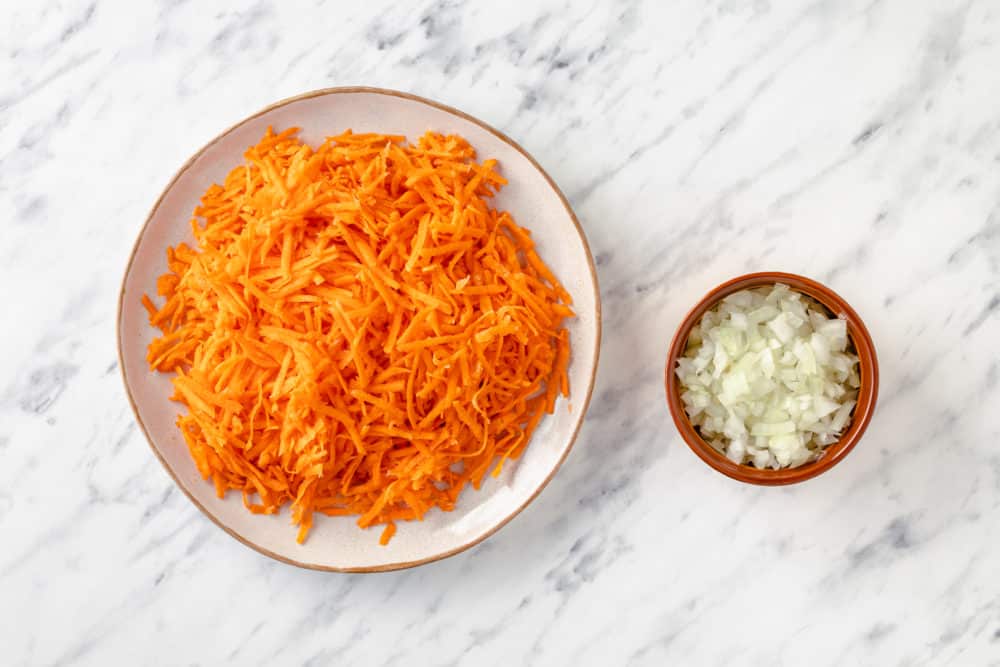 grated carrots on a white plate and chopped onions in a red dish.