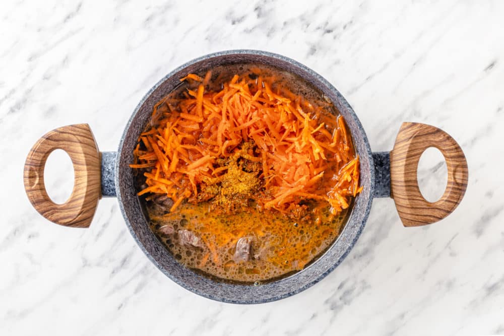 beef stock carrots and spices in a pot all together with wooden handles.