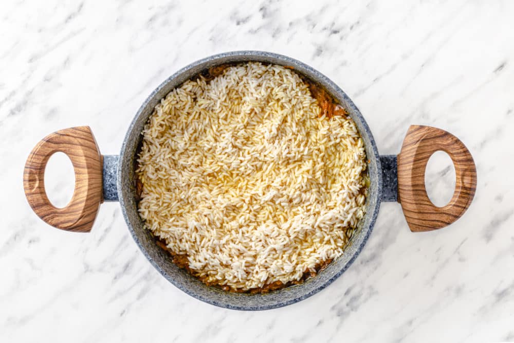 ingredients in a grey pot with rice on top.