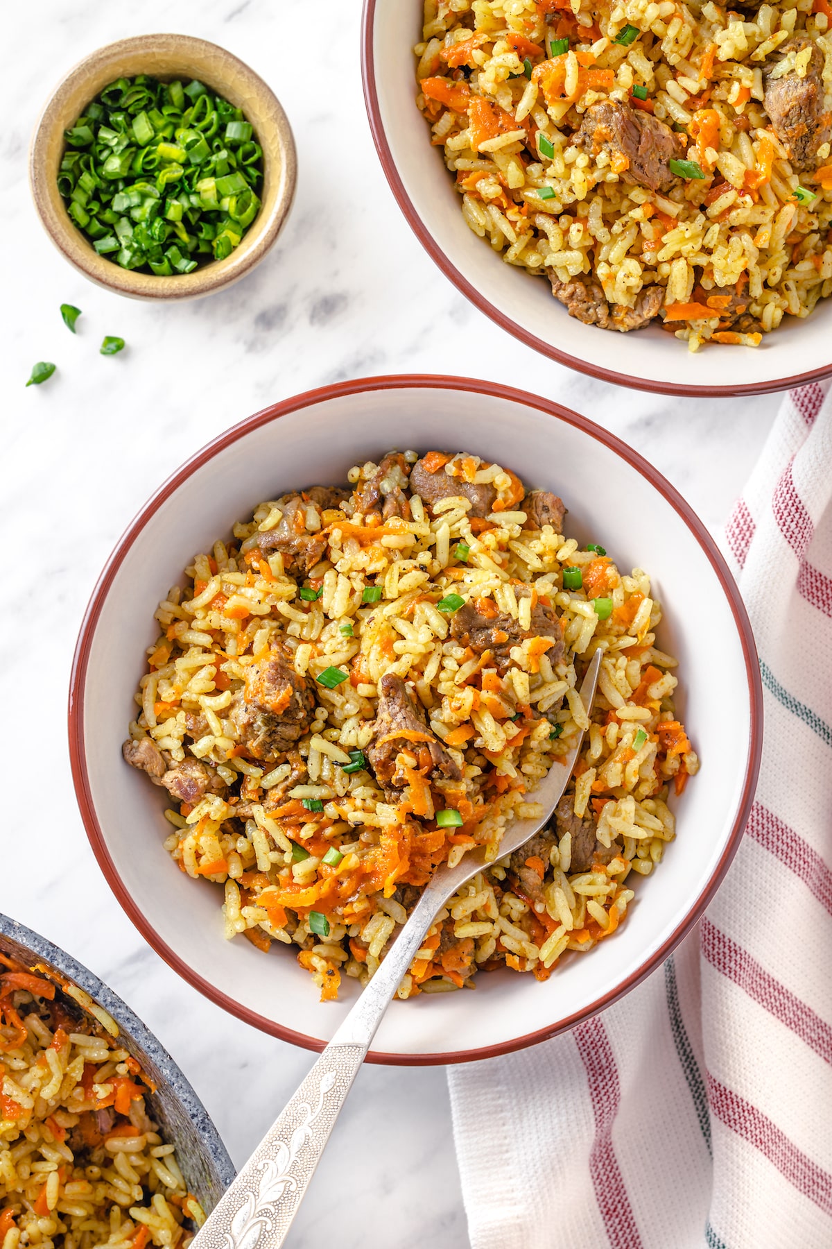 white bowl with cooked rice and beef plov with greens on the side and towel.