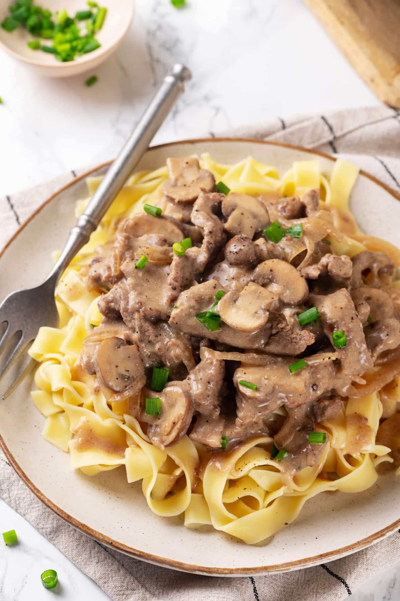 easy beef stroganoff with mushrooms served over egg noodles on a white plate with a fork beside it