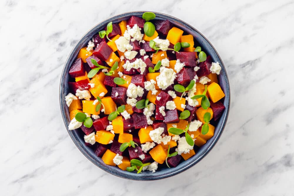 Cubed red and golden beets in a bowl with feta cheese and microgreens sprinkled on top.