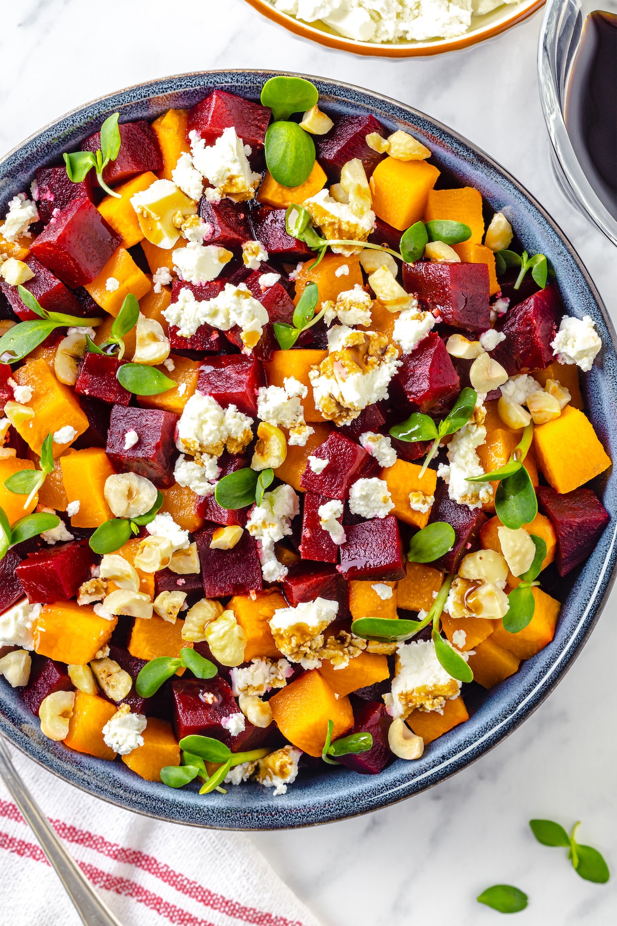 red and golden beets cubed in a grey bowl with goat cheese crumble and hazelnuts with microgreens.