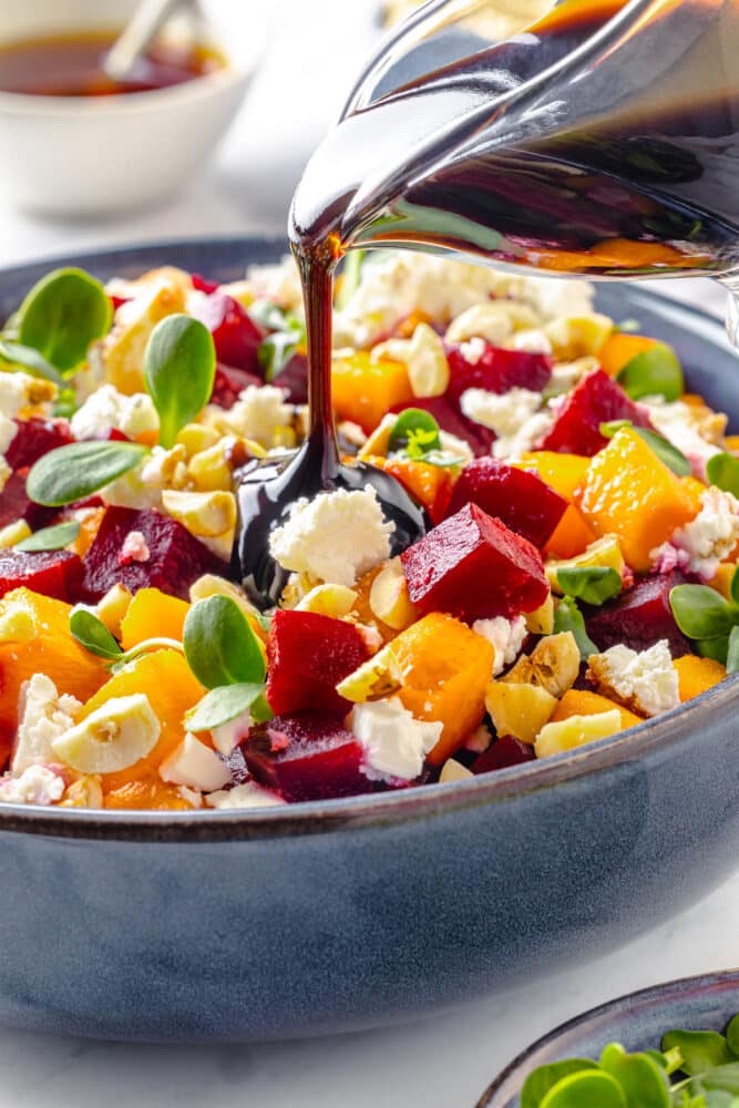 Beet salad in a blue bowl with balsamic dressing being drizzled on top from a glass pitcher.