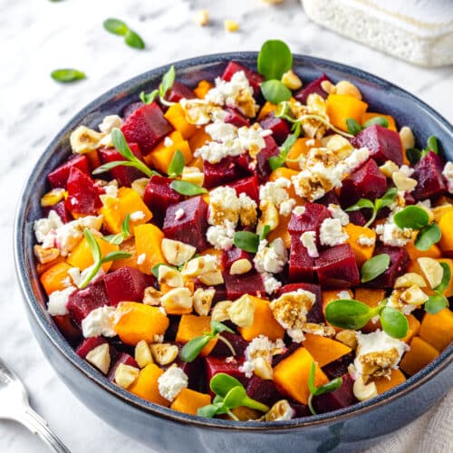 A blue bowl filled with beet salad with mixed in goat cheese hazelnuts and microgreens.