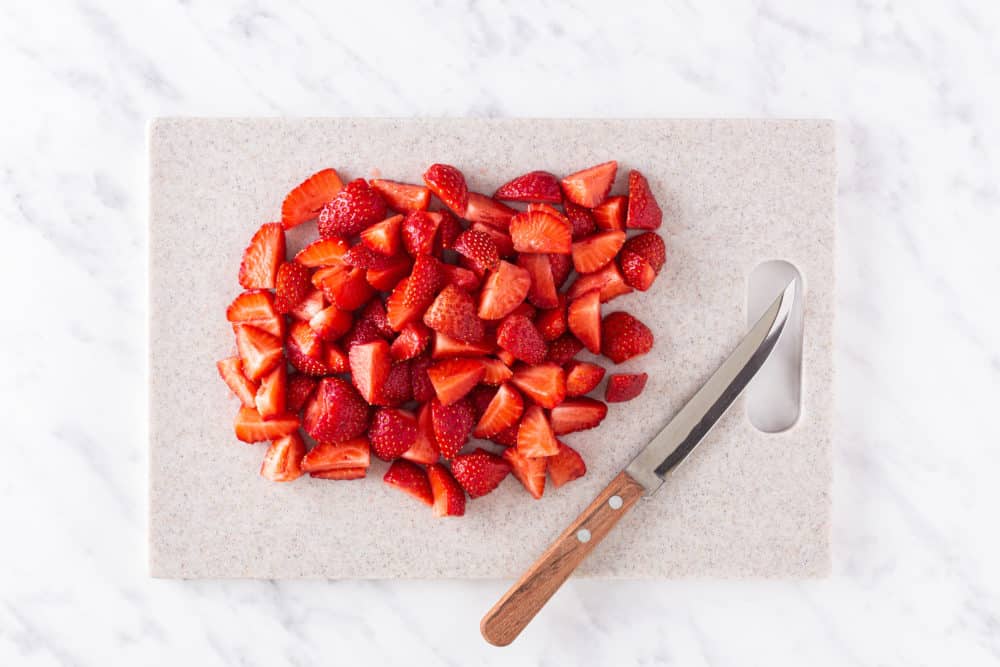 chopped strawberries on a cutting board with a knife.