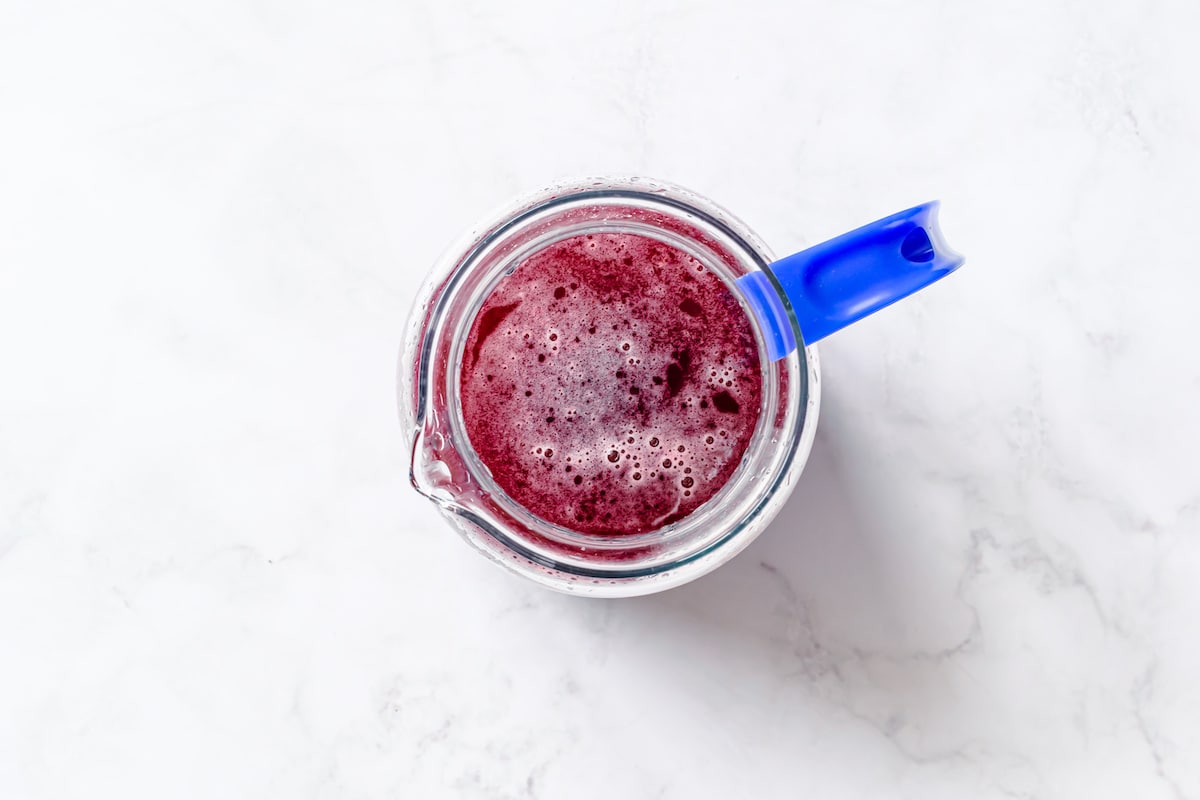 Fresh boiled blueberry, mint, honey, lime juice and zest, in a clear pitcher with blue handle.