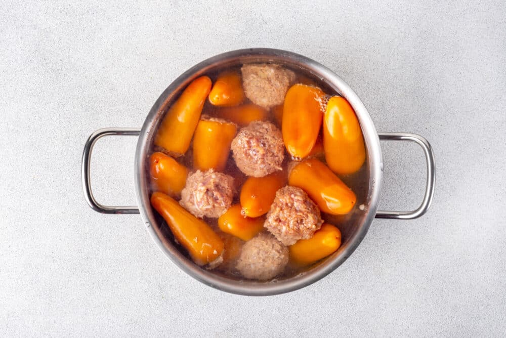 Boiling meatballs and mini peppers in a pot of water.