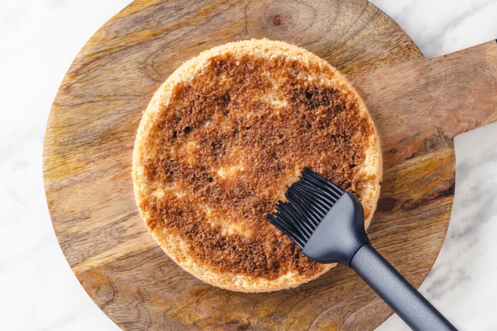 Brushing a cake layer with a coffee mixture atop a wooden board.