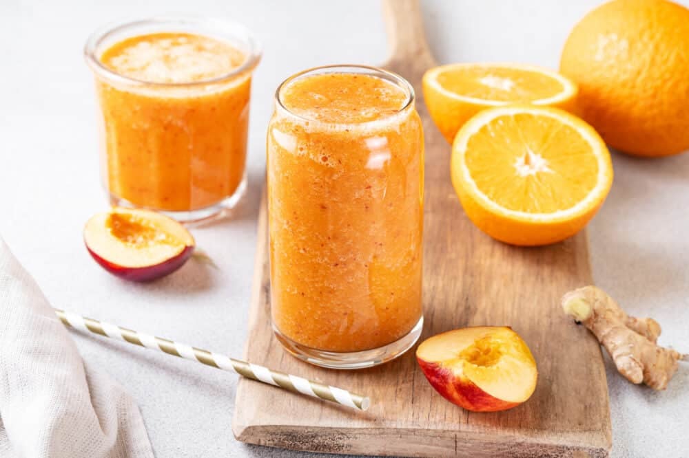 Carrot and nectarine smoothie with apricot in a glass with a straw on the side.