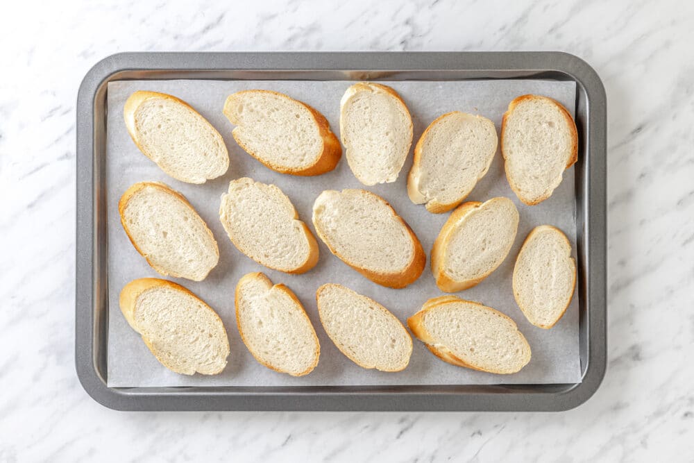 baguette slices spread out on a tray.