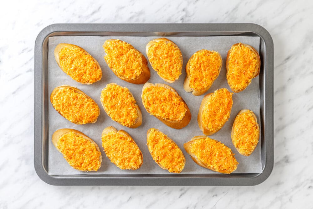 a baking tray with ready to bake bread slices and carrot cheese mix.