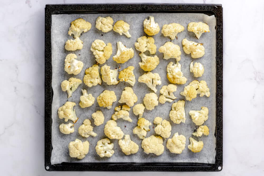 cauliflower florets mixed with salt and olive oil on a baking sheet with parchment paper.