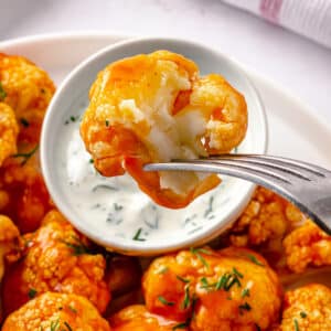 baked and mixed with buffalo sauce cauliflower on a silver fork dipping in greek yogurt dressing.