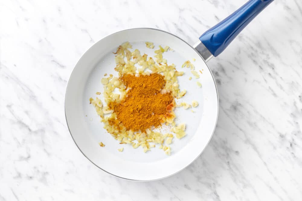 spices added to onion and garlic sauteeing in a skillet.