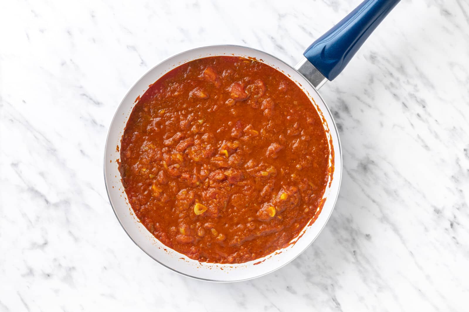 canned tomatoes added to spices and veggies cooking in a skillet.