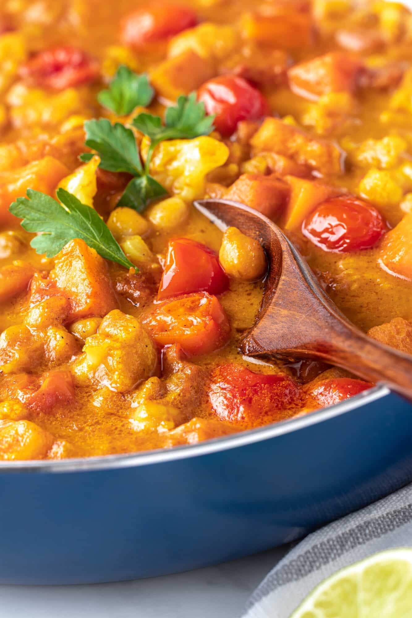 close up photo of a wooden spoon in cauliflower and chickpea curry.