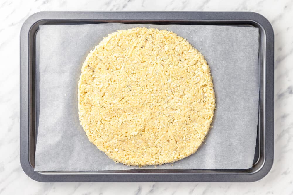 cauliflower pizza crust formed into a circle on a baking sheet with parchment paper.