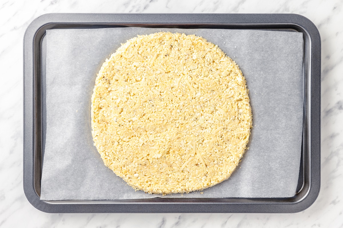 cauliflower pizza crust formed into a circle on a baking sheet with parchment paper. 