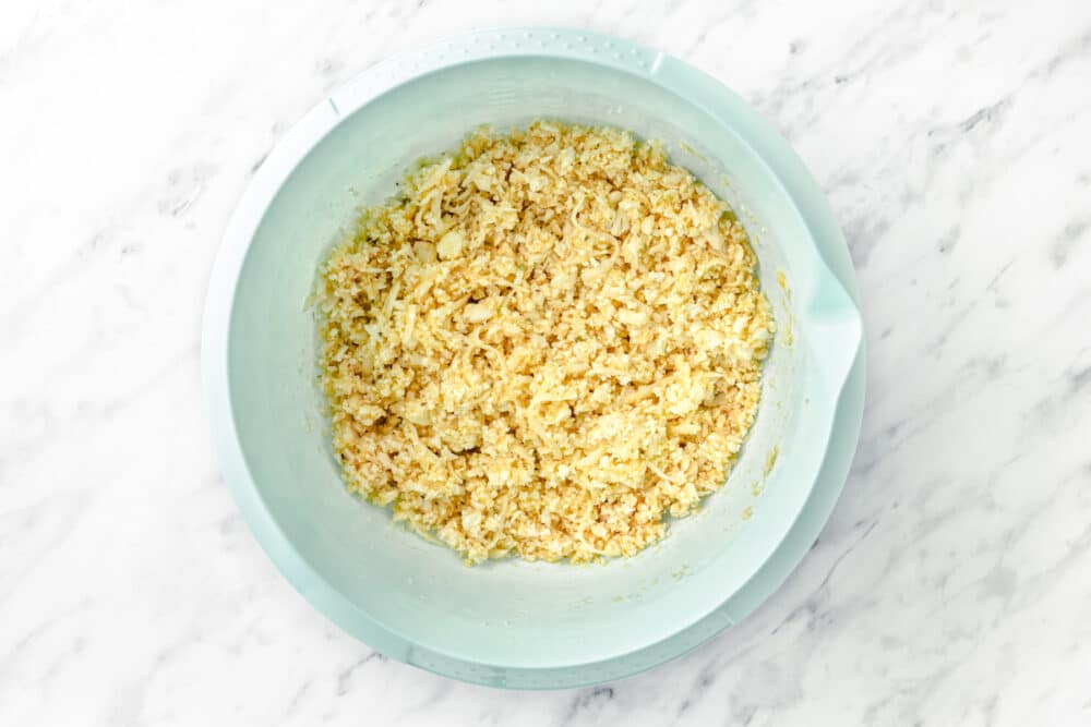 cauliflower pizza crust mixed in a blue mixing bowl on marble background.