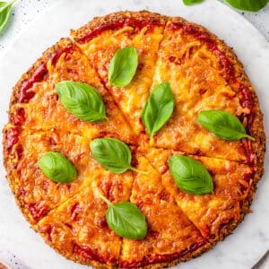 round cauliflower crust pizza with red sauce and fresh basil on marble background.