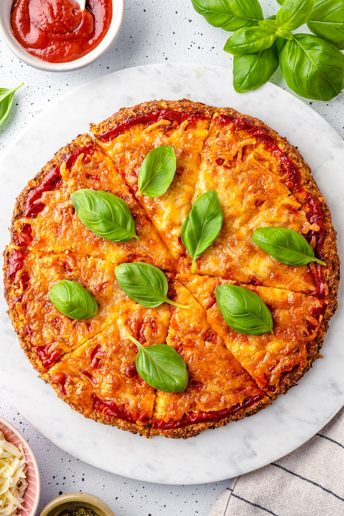 round cauliflower crust pizza with red sauce and fresh basil on marble background.