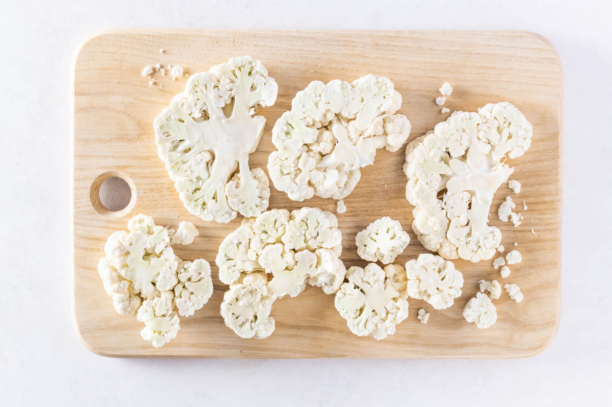 raw cauliflower steak slices on a wooden cutting board