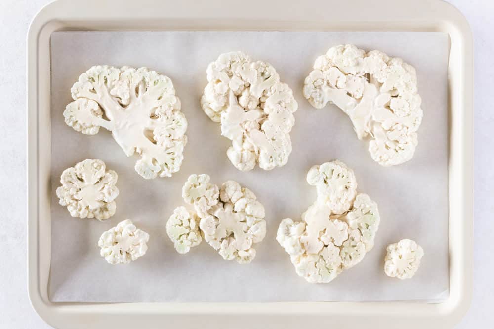 raw cauliflower steak slices on a baking tray.