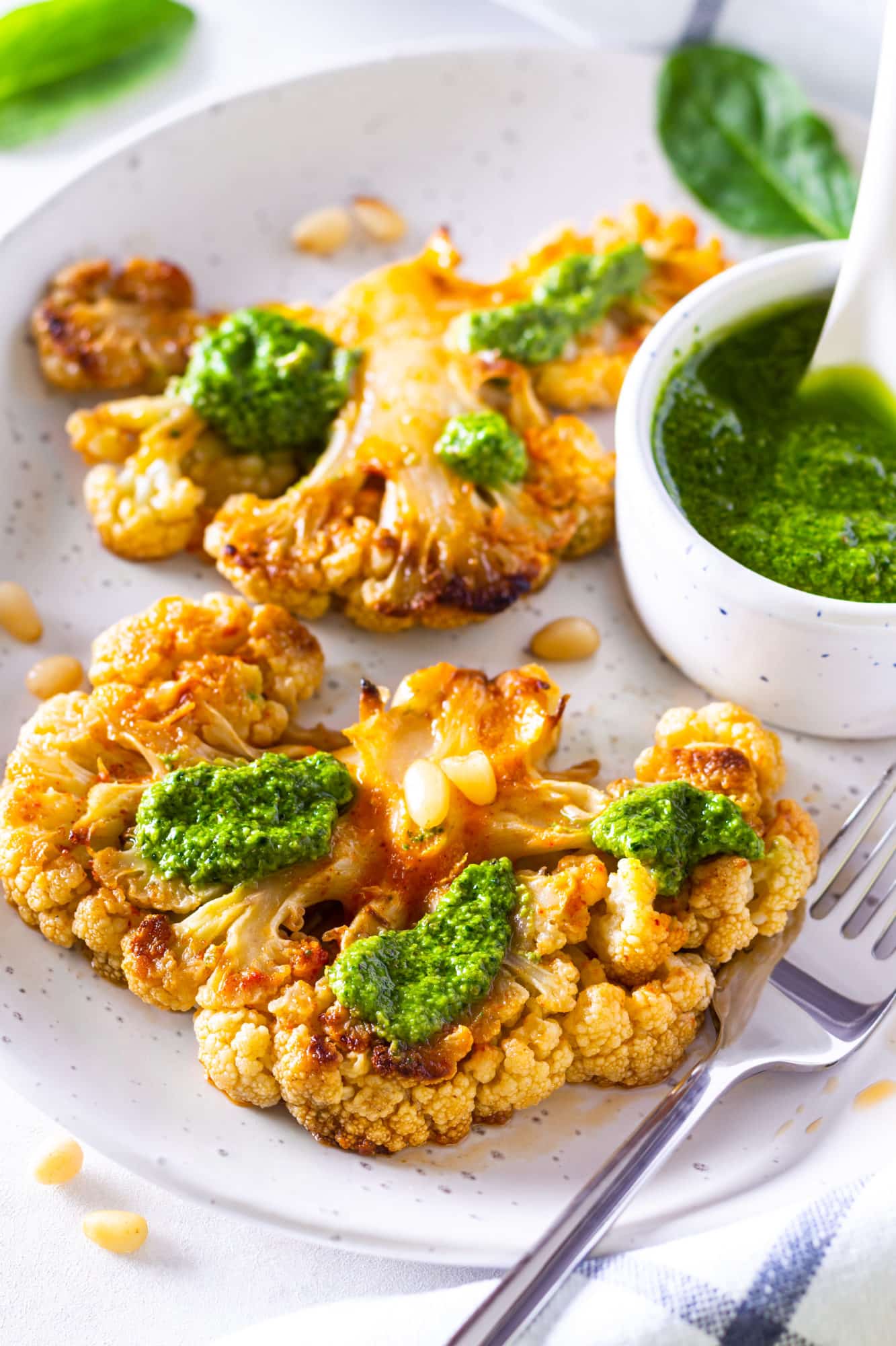 a silver fork on a grey plate with roasted cauliflower steak and pesto on it.