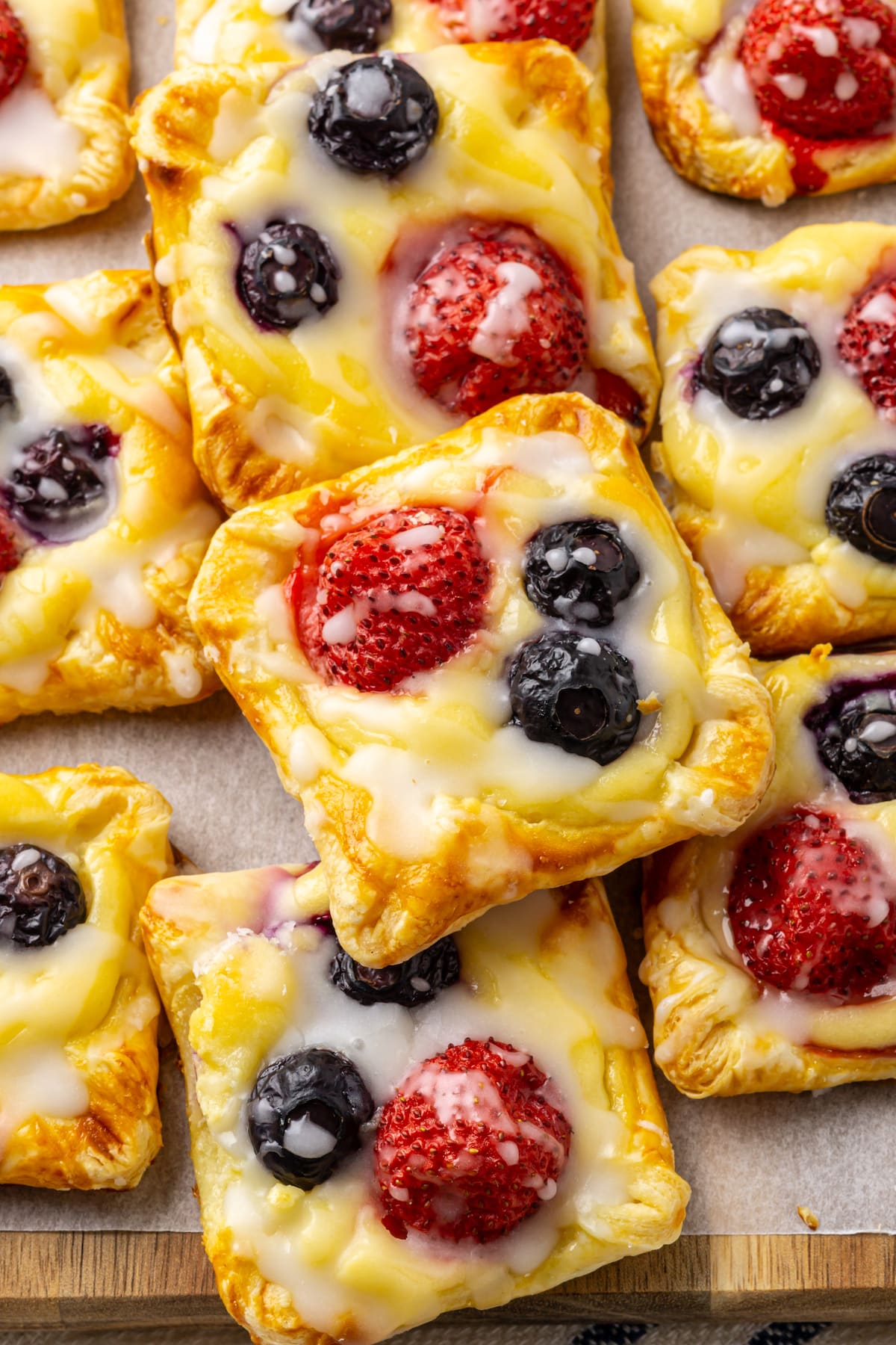 Cheese danishes with berries on a wooden board with parchment paper.