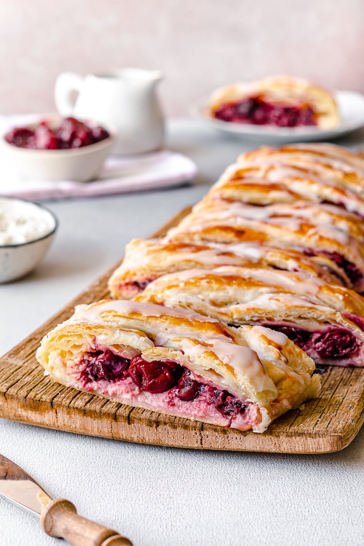 cherry cheese danish with glaze on top on a wooden board cut up into slices.