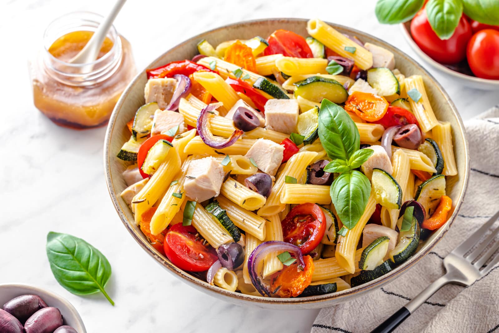 Chicken pasta salad bowl with roasted vegetables and basil.