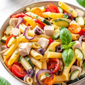 Chicken pasta salad in a bowl with basil leaves on top.