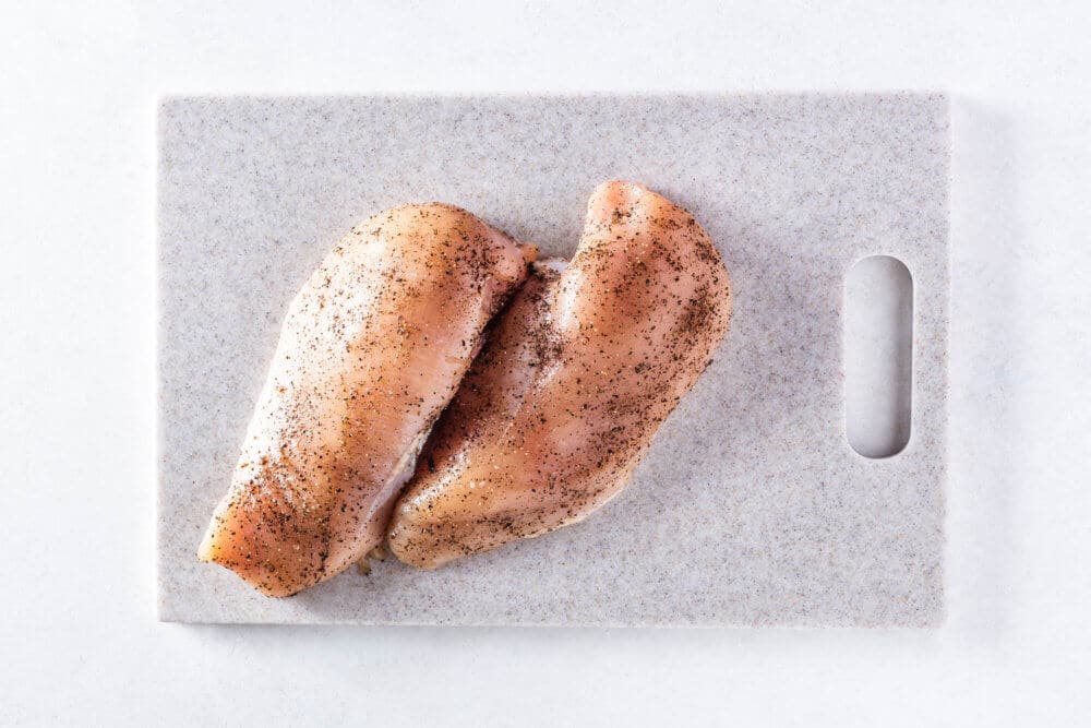 two raw chicken breasts on a grey cutting board.