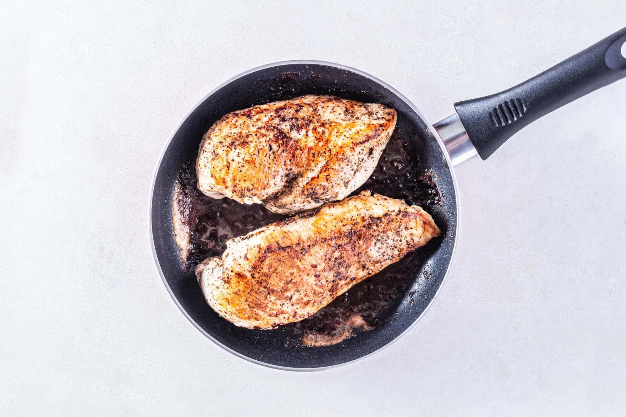 Chicken breasts cooking in a skillet with butter.