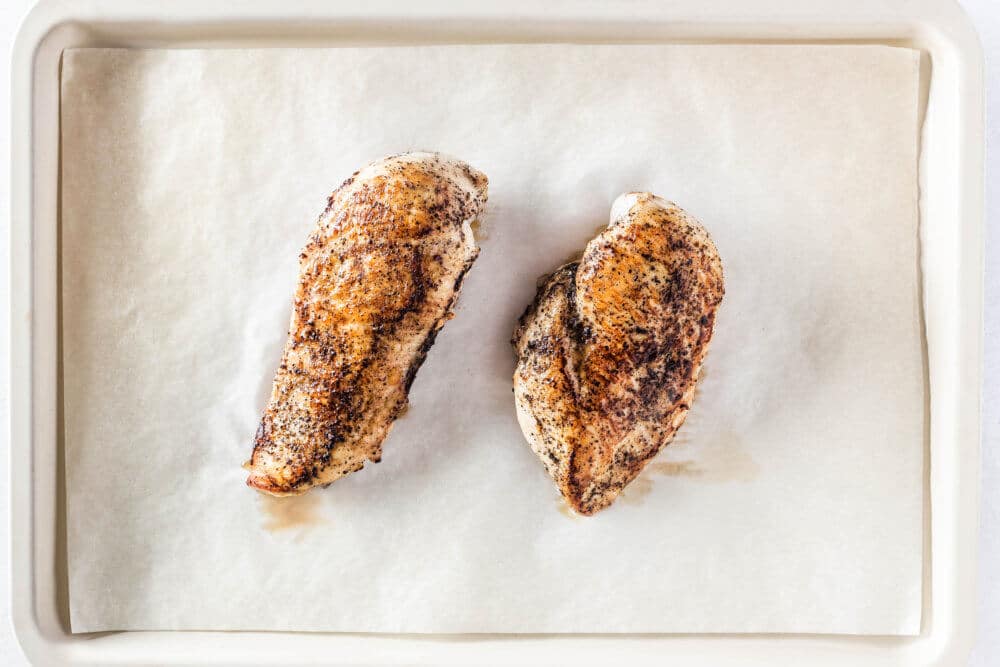 cooked chicken breast on parchment paper on a baking tray.