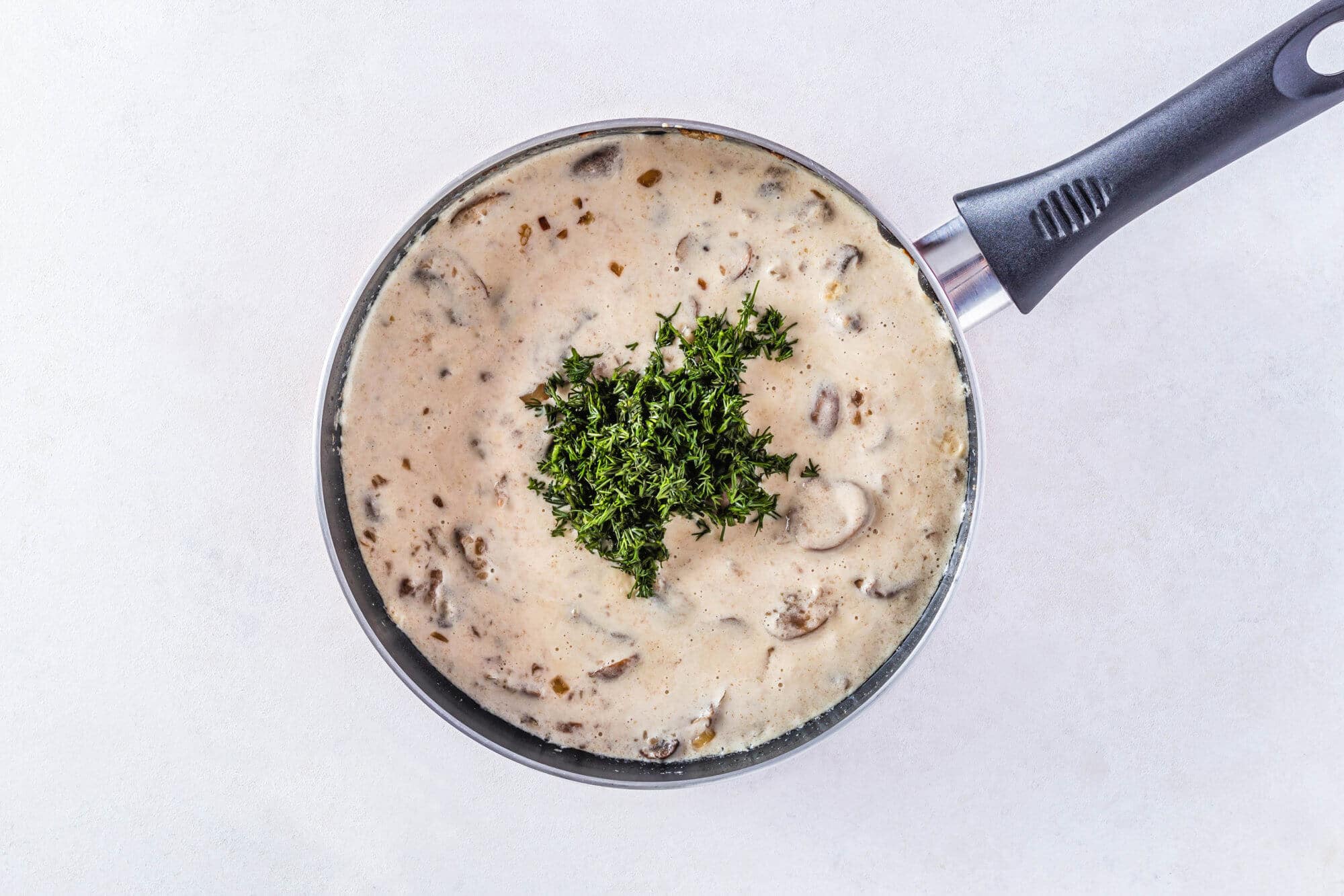 Fresh dill added atop mushroom sauce cooking in a skillet.