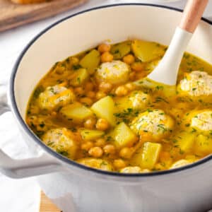 Chickpea and meatball soup in a pot with a spoon for mixing.