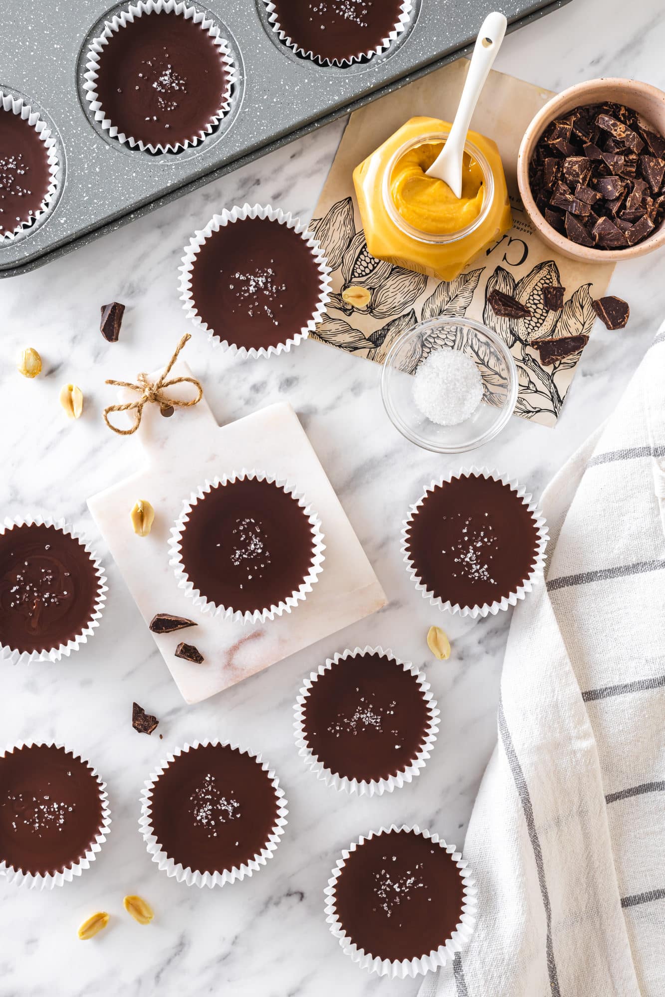 top view of peanut butter cups with salt on top with peanut butter and chocolate in separate bowls on the side.