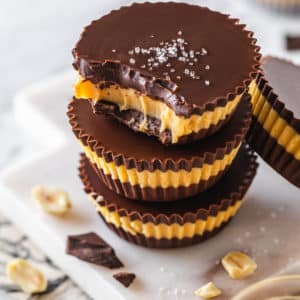 Dark chocolate peanut butter cups stacked with the top cup bitten out with salt on it.