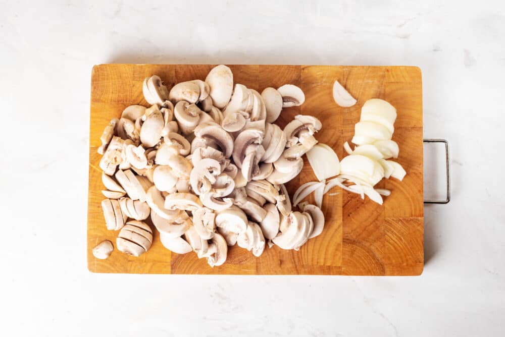 Chopped mushrooms and onions on a cutting board.