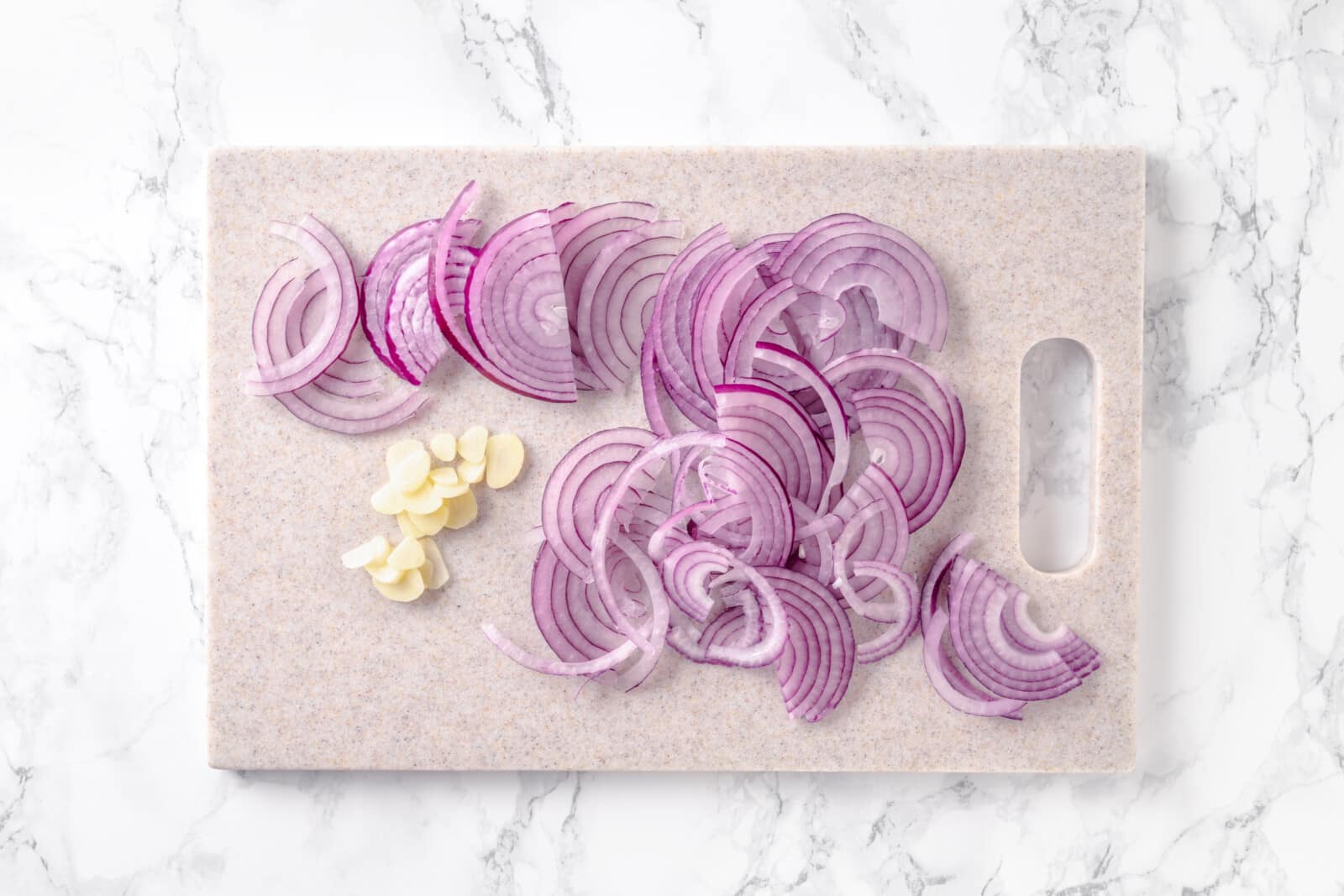 Chopped garlic and red onion on a cutting board.