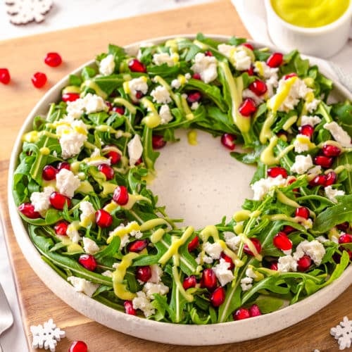 a green salad on a white plate on a cutting board with pomegranate seeds sprinkled on top.