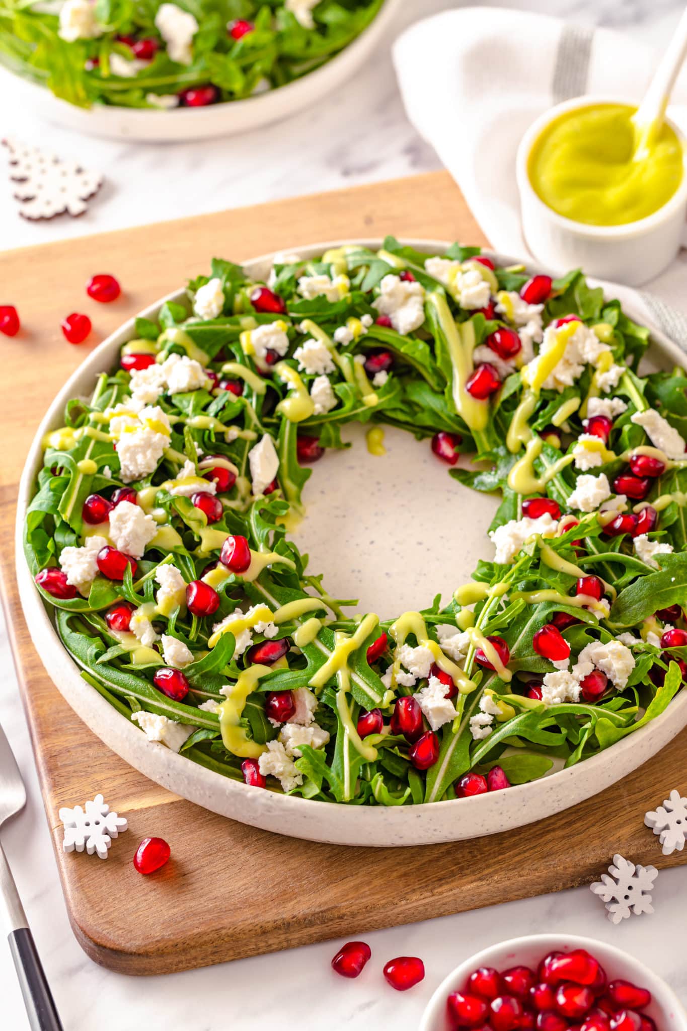 a green salad on a white plate on a cutting board with pomegranate seeds sprinkled on top.